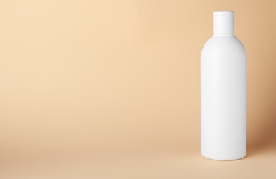 Photo of Bottle of shampoo on beige background, space for text