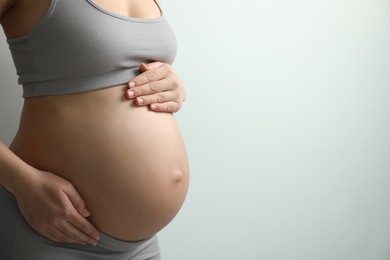 Photo of Pregnant young woman touching belly on light background, closeup. Space for text