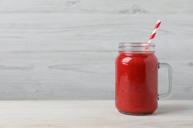 Photo of Mason jar with delicious berry smoothie on white wooden table. Space for text