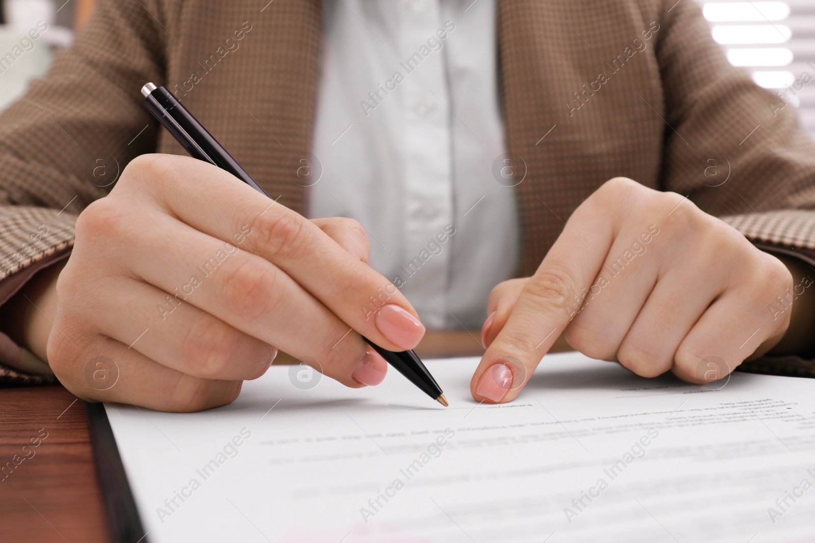 Photo of Woman signing document at wooden table, closeup