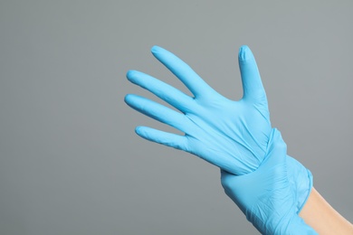 Photo of Doctor wearing medical gloves on grey background, closeup. Space for text