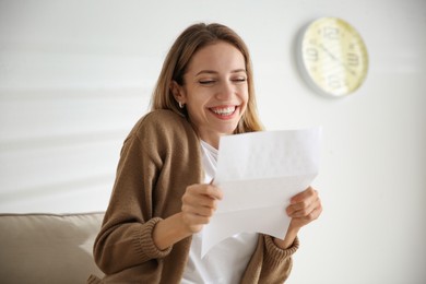 Photo of Excited woman reading letter on sofa at home