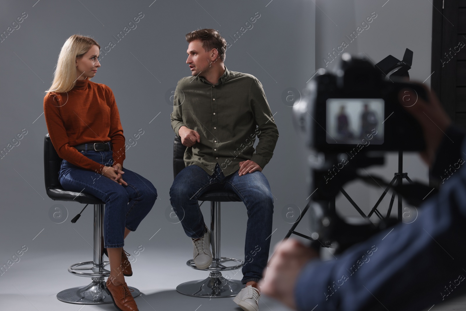 Photo of Casting call. Man and woman performing while camera operator filming them against grey background in studio