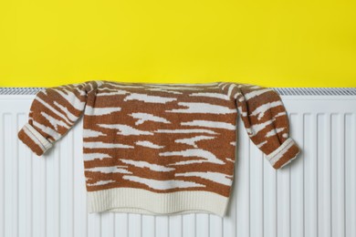 Photo of Knitted sweater on heating radiator near yellow wall