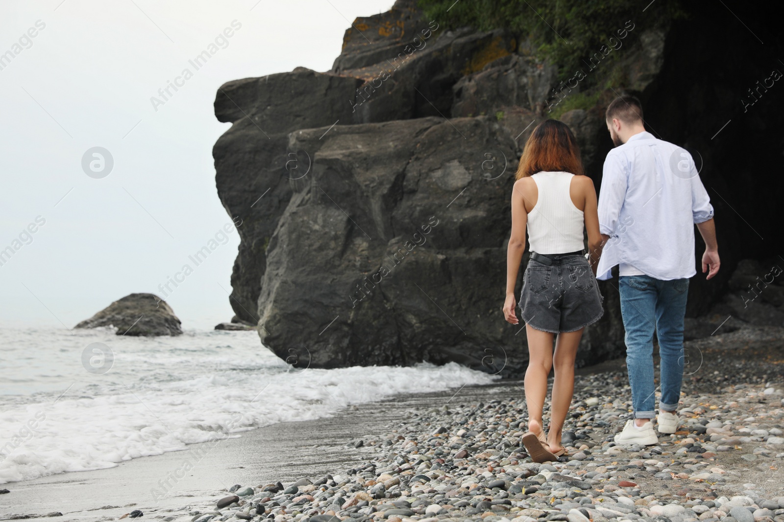 Photo of Young couple walking on beach near sea, back view. Space for text