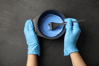 Photo of Woman preparing dye for hair coloring at black stone table, top view