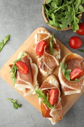 Photo of Tasty sandwiches with cured ham, tomatoes and arugula on grey table, flat lay