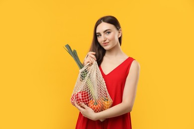 Woman with string bag of fresh vegetables on orange background