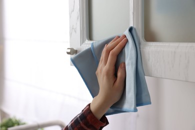 Photo of Woman with microfiber cloth cleaning white cabinet in kitchen, closeup