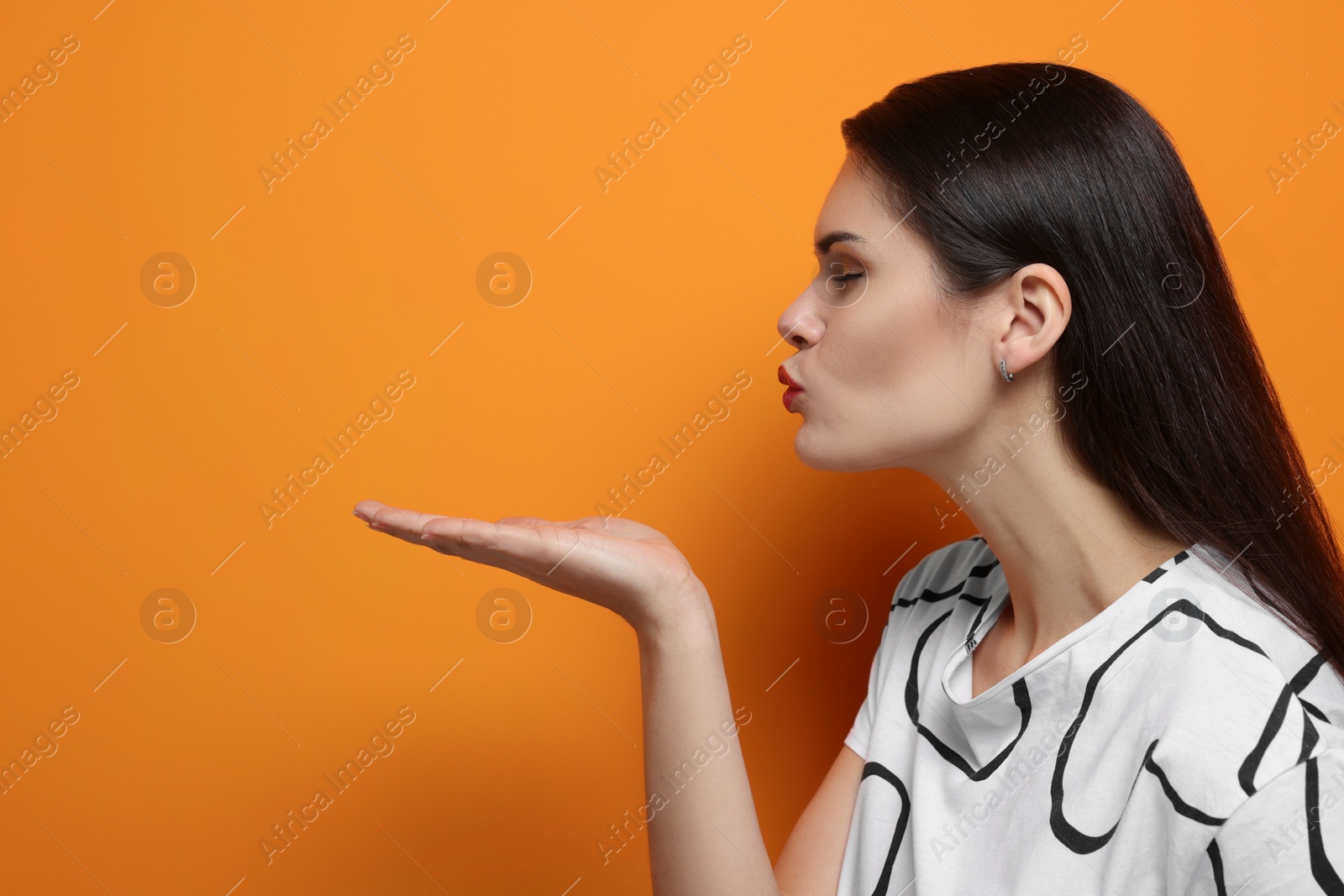 Photo of Beautiful young woman blowing kiss on orange background. Space for text