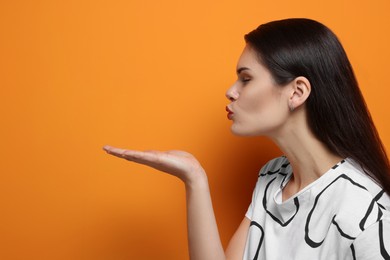 Beautiful young woman blowing kiss on orange background. Space for text