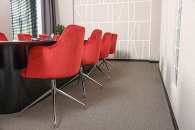 Photo of Stylish red office chairs and large table in empty conference room