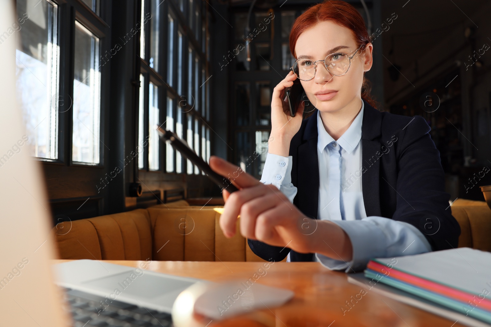 Photo of Young female student with laptop talking on phone while studying at table in cafe