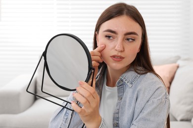 Photo of Young woman with skin problem looking at mirror indoors