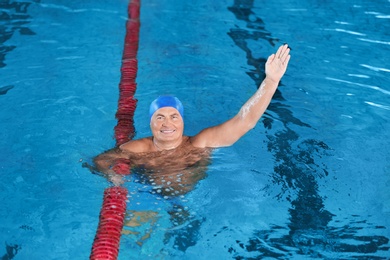 Sportive senior man doing exercises in indoor swimming pool