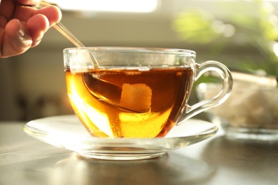 Photo of Woman adding sugar into cup of tea at table, closeup