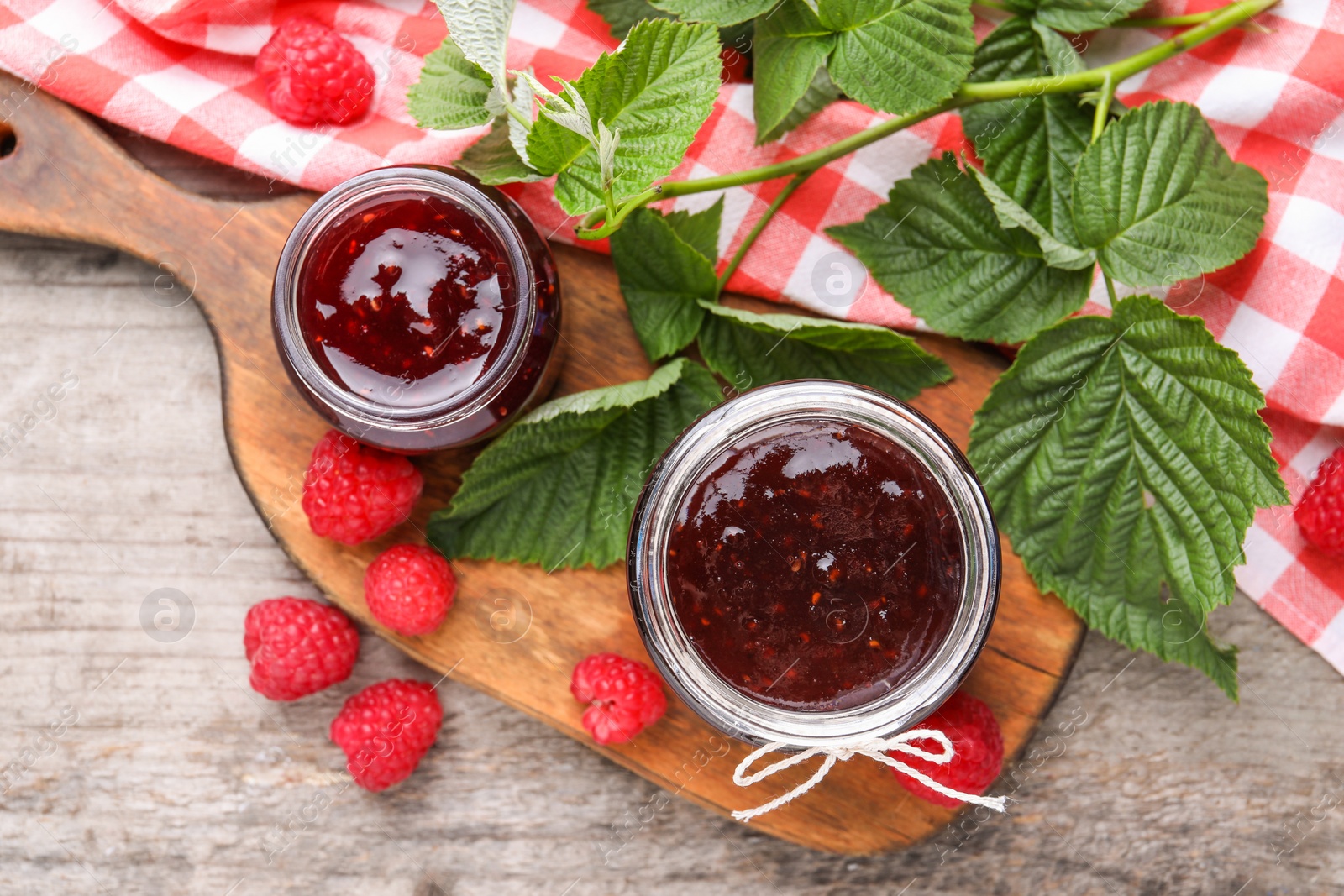 Photo of Delicious raspberry jam, fresh berries and green leaves on wooden table, flat lay