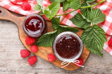 Delicious raspberry jam, fresh berries and green leaves on wooden table, flat lay