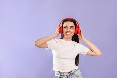 Teenage girl listening music with headphones on violet background
