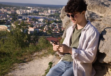 Photo of Travel blogger in sunglasses using smartphone outdoors