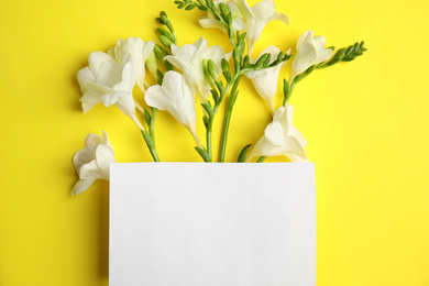 Photo of Beautiful spring freesia flowers and blank card on yellow background, flat lay. Space for text