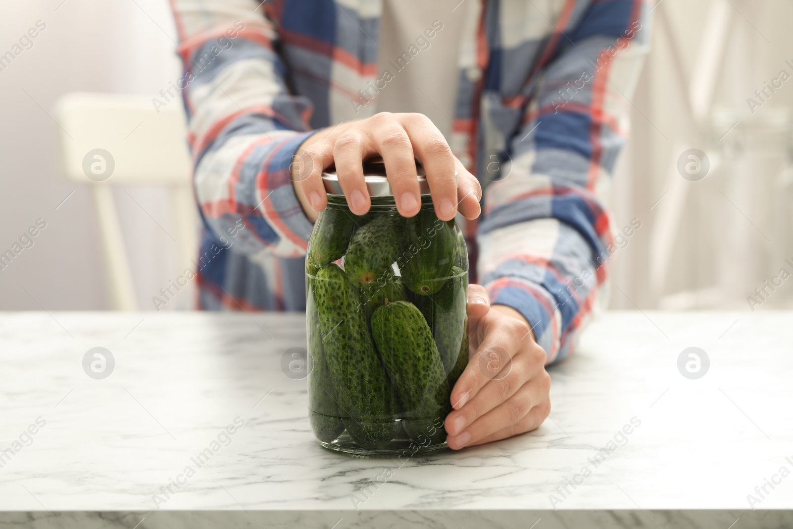 Photo of Woman pickling glass jar of cucumbers at white marble kitchen table, closeup