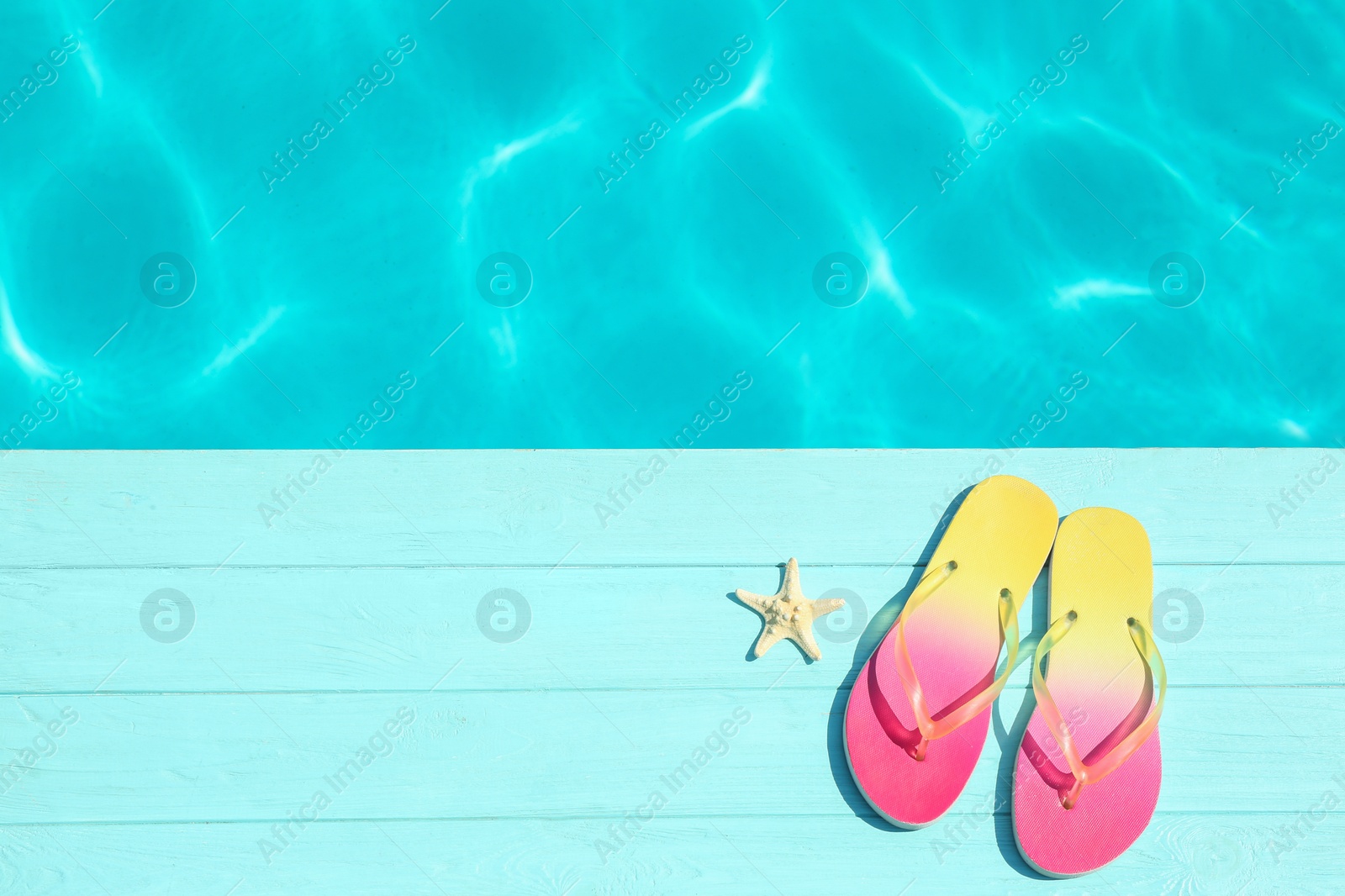 Photo of Slippers and starfish on wooden deck near swimming pool, top view with space for text. Beach accessory