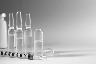 Pharmaceutical ampoules and syringe on light grey background. Space for text