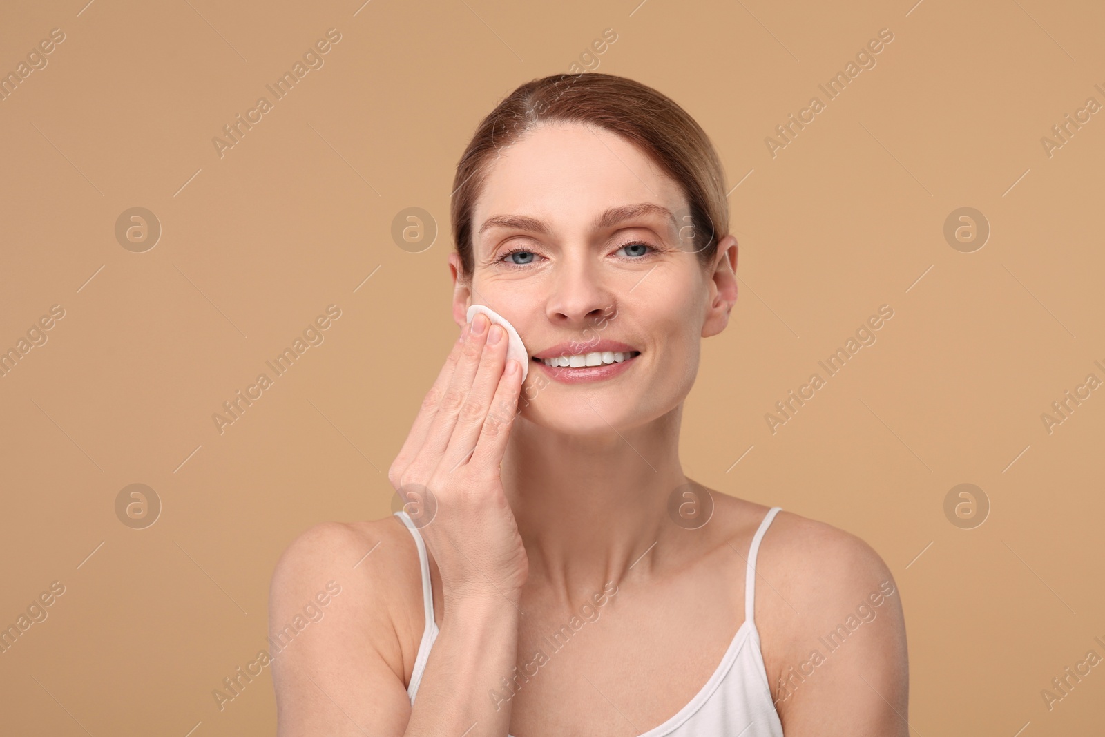 Photo of Beautiful woman removing makeup with cotton pad on beige background