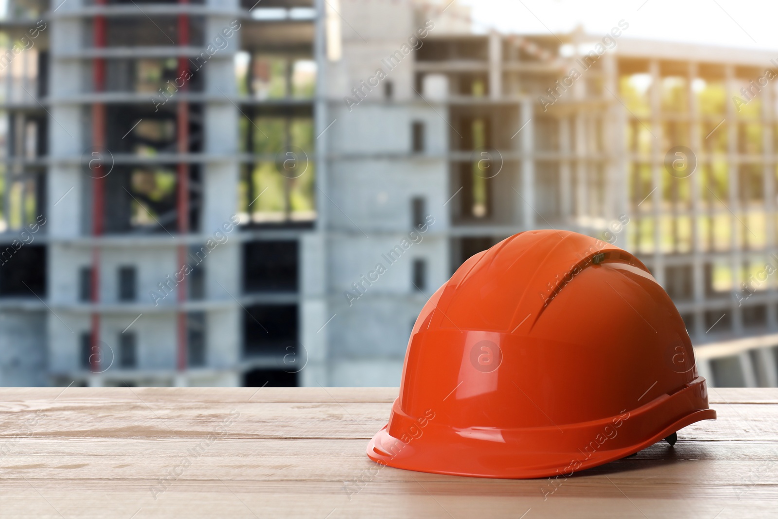 Image of Safety equipment. Hard hat on wooden surface near unfinished building outdoors, space for text