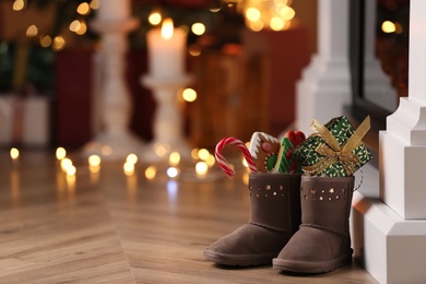 Photo of Boots filled with sweets and gift on floor in room, space for text. Saint Nicholas Day