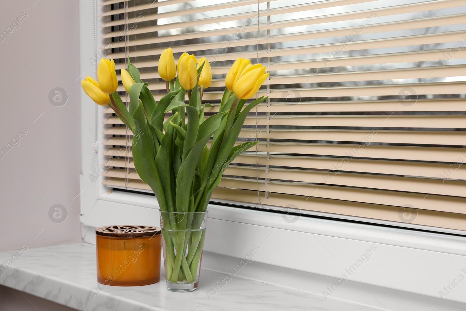 Photo of Wonderful tulips and candle on window sill indoors, space for text. Spring atmosphere