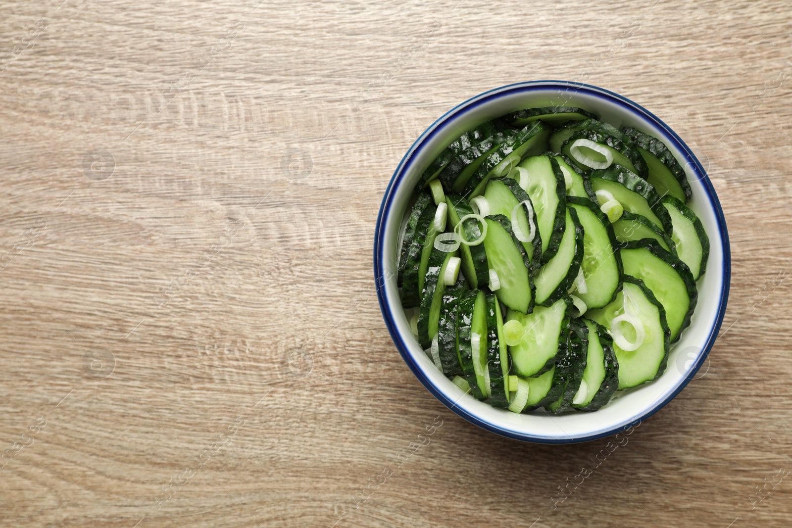 Photo of Delicious salad with cucumbers and green onion in bowl on wooden table, top view. Space for text