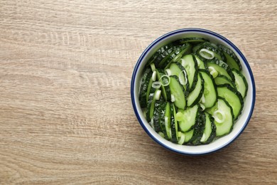 Photo of Delicious salad with cucumbers and green onion in bowl on wooden table, top view. Space for text