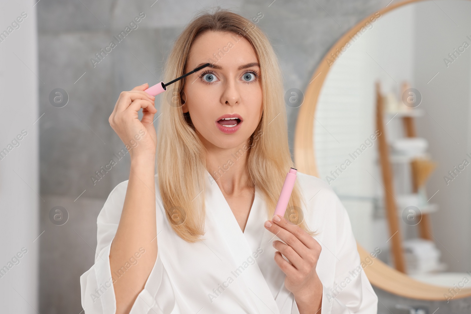 Photo of Beautiful emotional woman applying mascara in bathroom