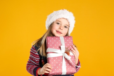 Photo of Cute child in Santa with Christmas gift on yellow background