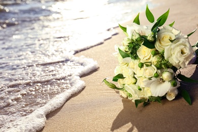 Photo of Beautiful wedding bouquet on sandy beach near sea. Space for text