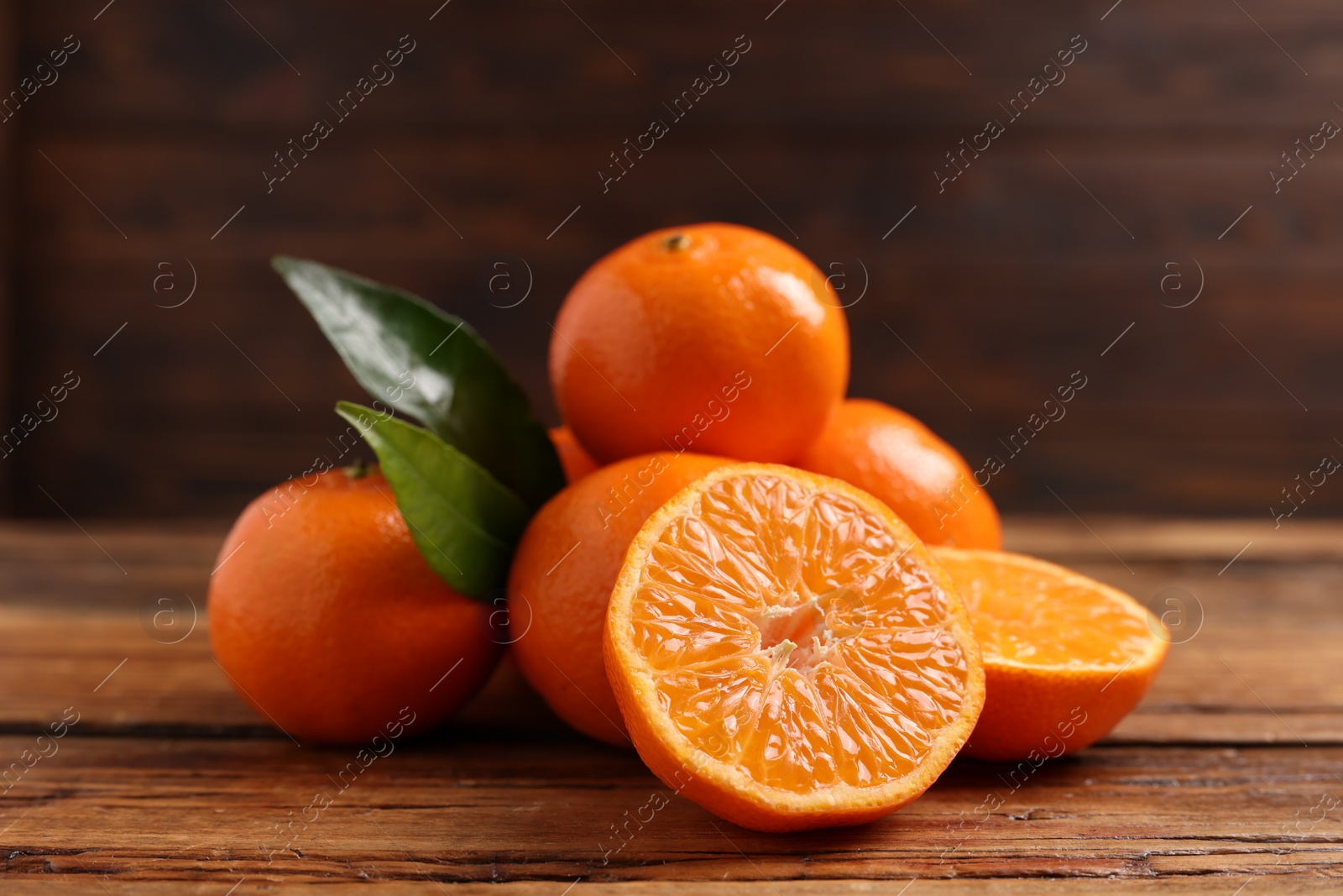 Photo of Fresh tangerines with green leaves on wooden table, closeup