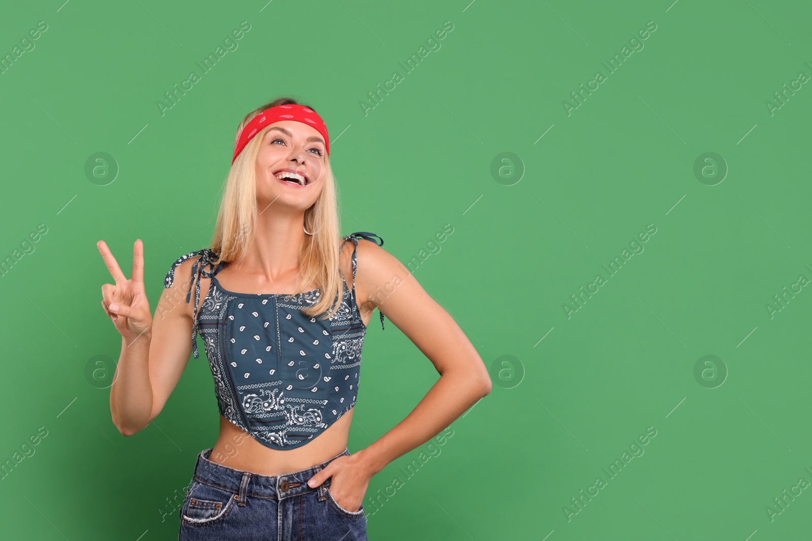 Photo of Portrait of happy hippie woman showing peace sign on green background. Space for text