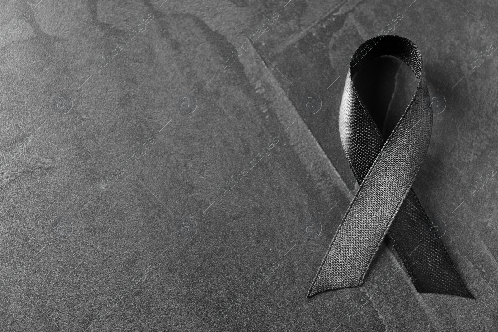 Photo of Black ribbon on dark grey stone surface, top view with space for text. Funeral symbol