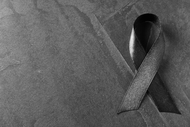 Photo of Black ribbon on dark grey stone surface, top view with space for text. Funeral symbol