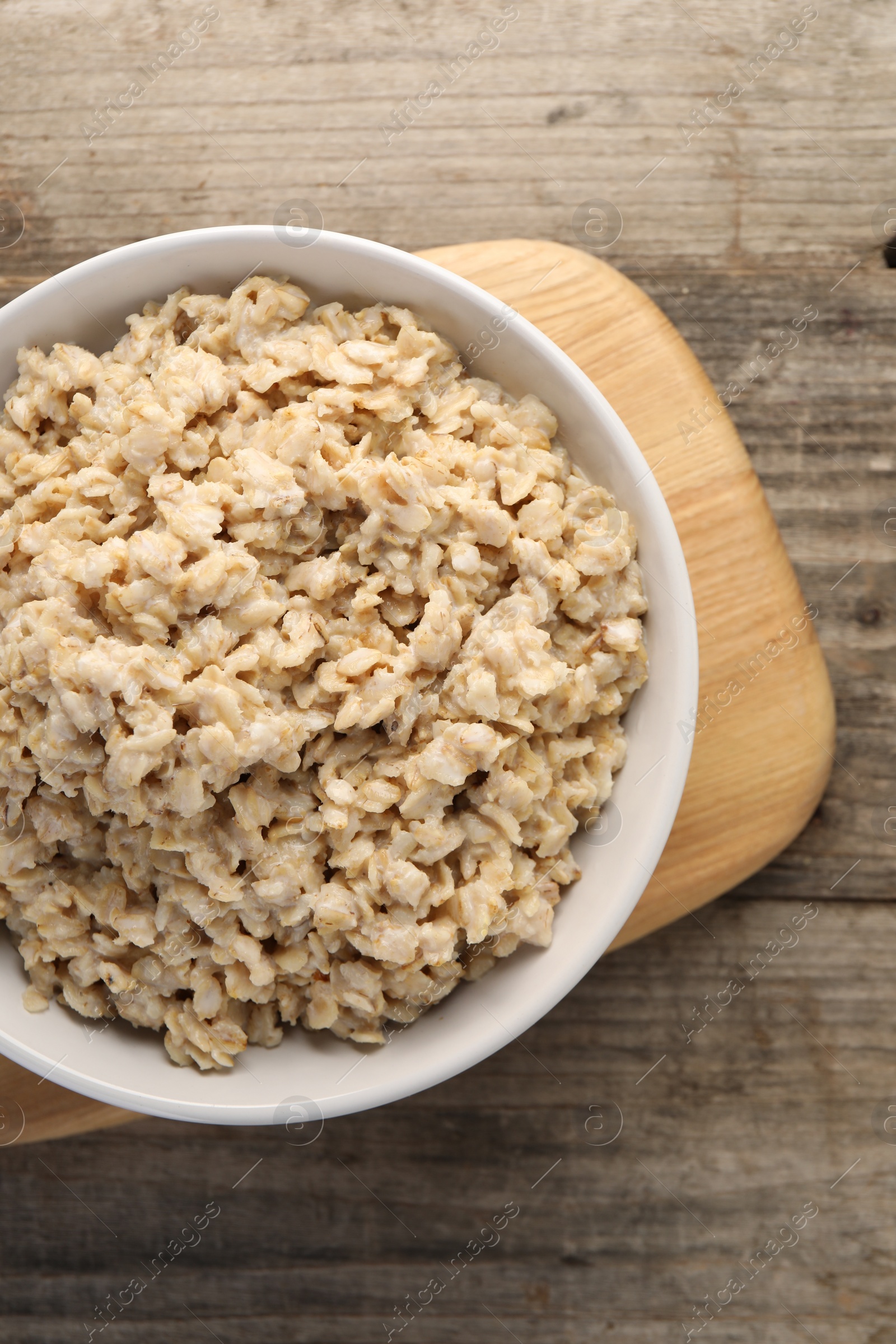 Photo of Tasty boiled oatmeal in bowl on wooden table, top view