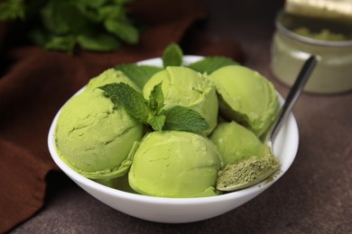 Photo of Tasty matcha ice cream and spoon with powder in bowl on brown table, closeup