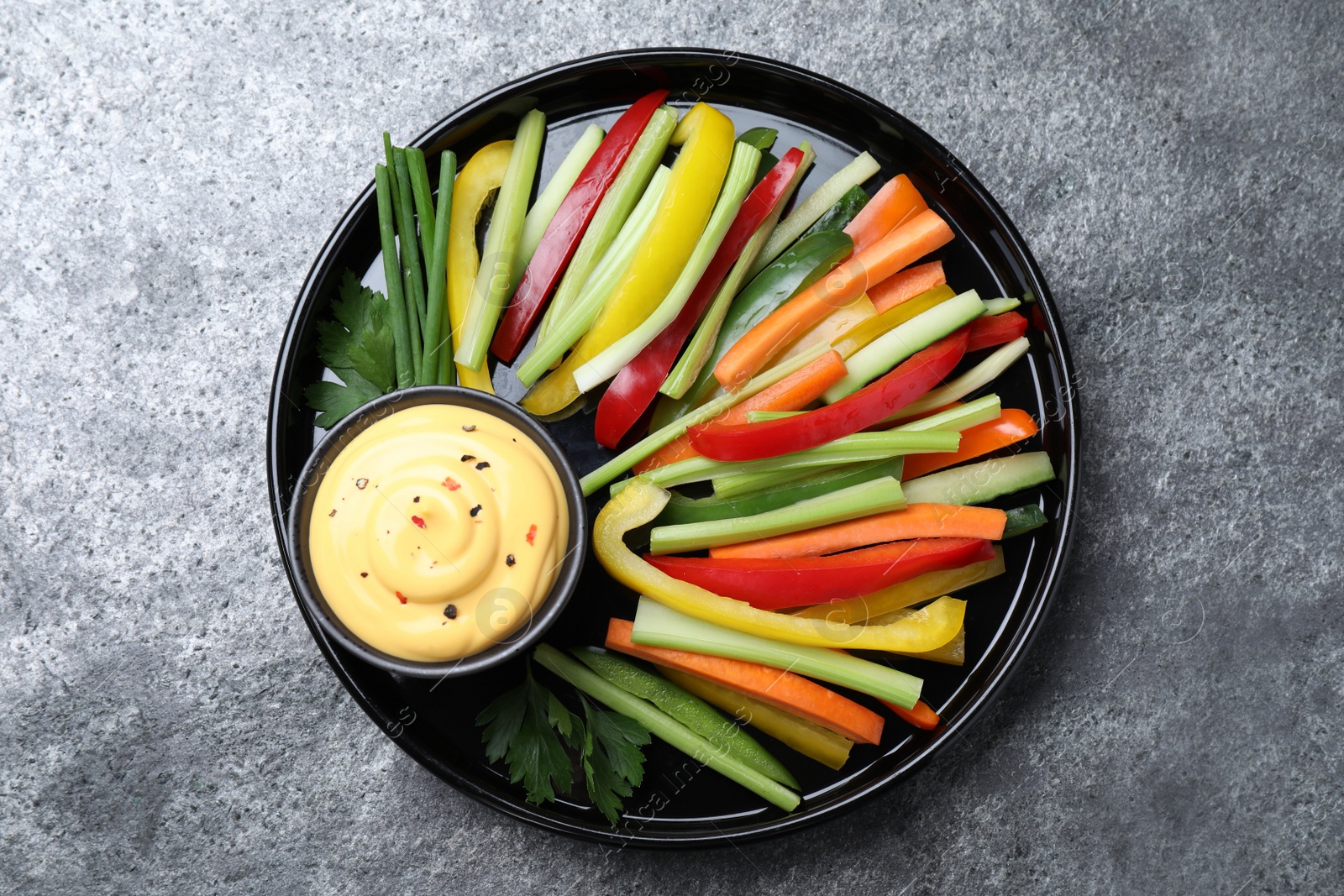 Photo of Fresh raw vegetable sticks and sauce on grey table, top view