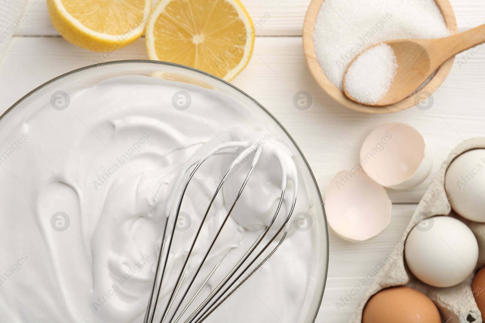 Photo of Bowl with whipped cream, whisk and ingredients on white wooden table, flat lay