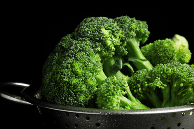 Photo of Fresh green broccoli in colander on black background, closeup