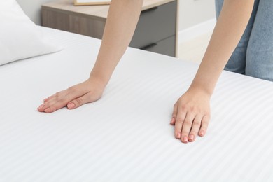 Woman touching white soft mattress on bed indoors, closeup