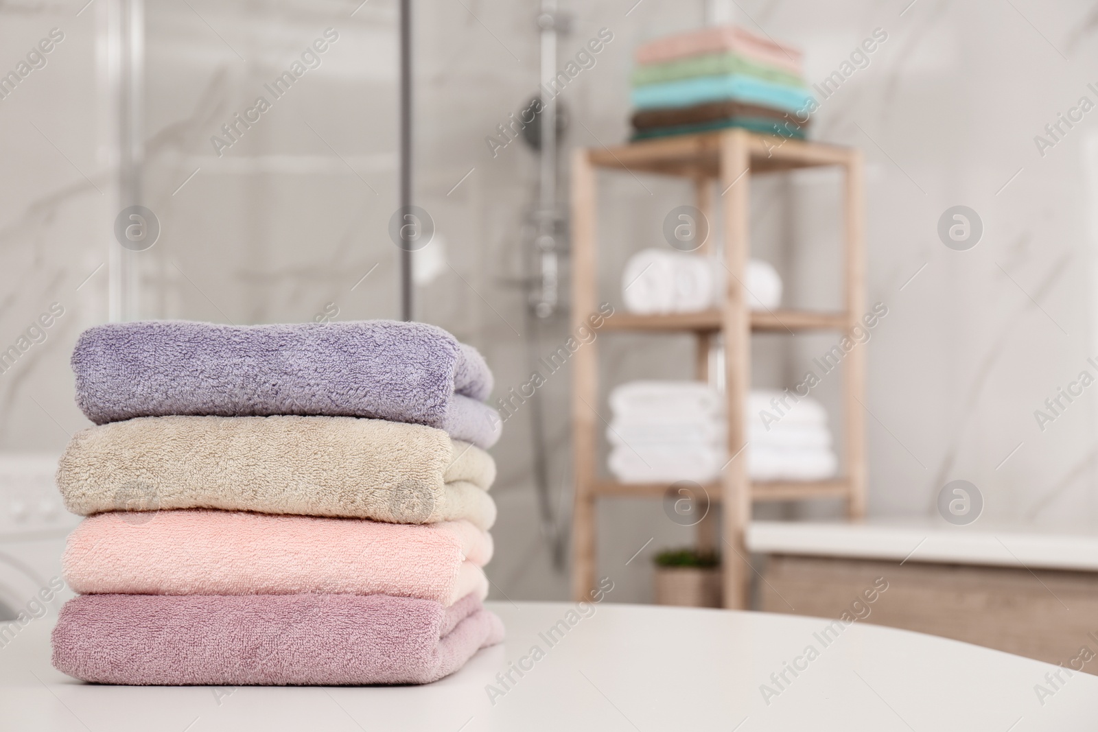 Photo of Stack of color towels on white table in bathroom. Space for text