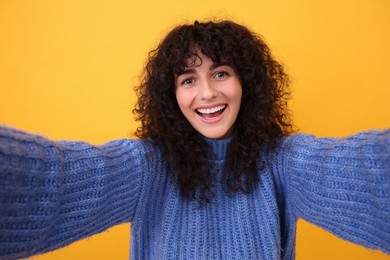 Photo of Beautiful young woman taking selfie on orange background