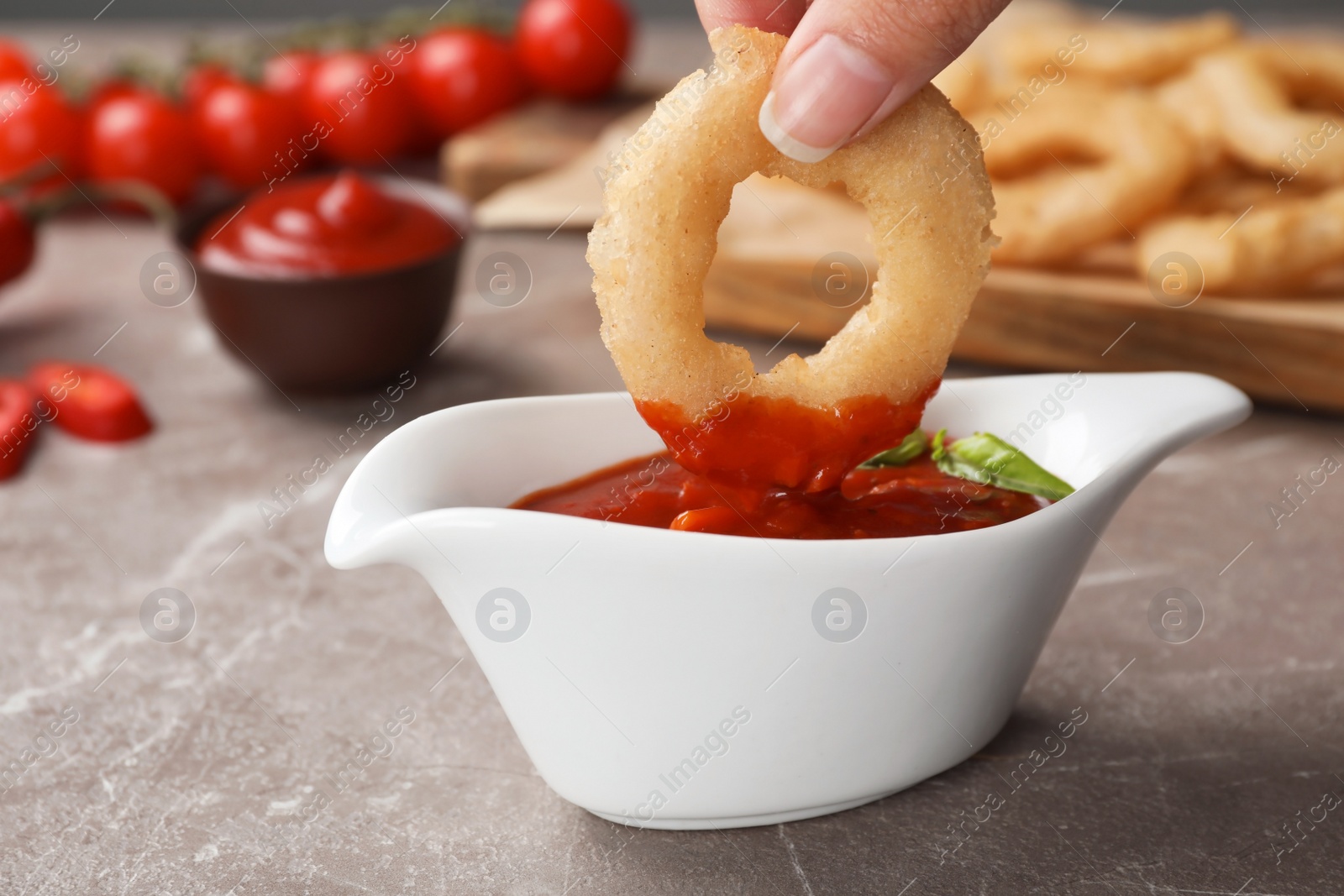 Photo of Woman dipping onion ring into hot chili sauce in gravy boat on table